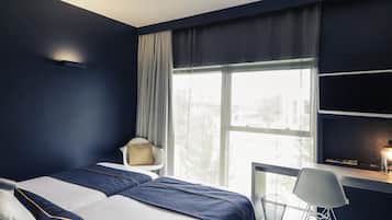 Habitación de hotel con cama, escritorio, silla y ventana con cortinas.