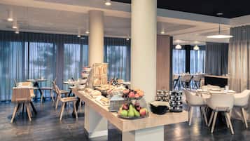 Un comedor moderno de hotel con barra de desayuno buffet, que incluye frutas, pasteles y bebidas.