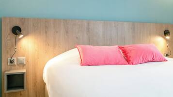 A bedroom with a wooden headboard, two bedside lamps, a white bed with pink pillows, and a small shelf unit.