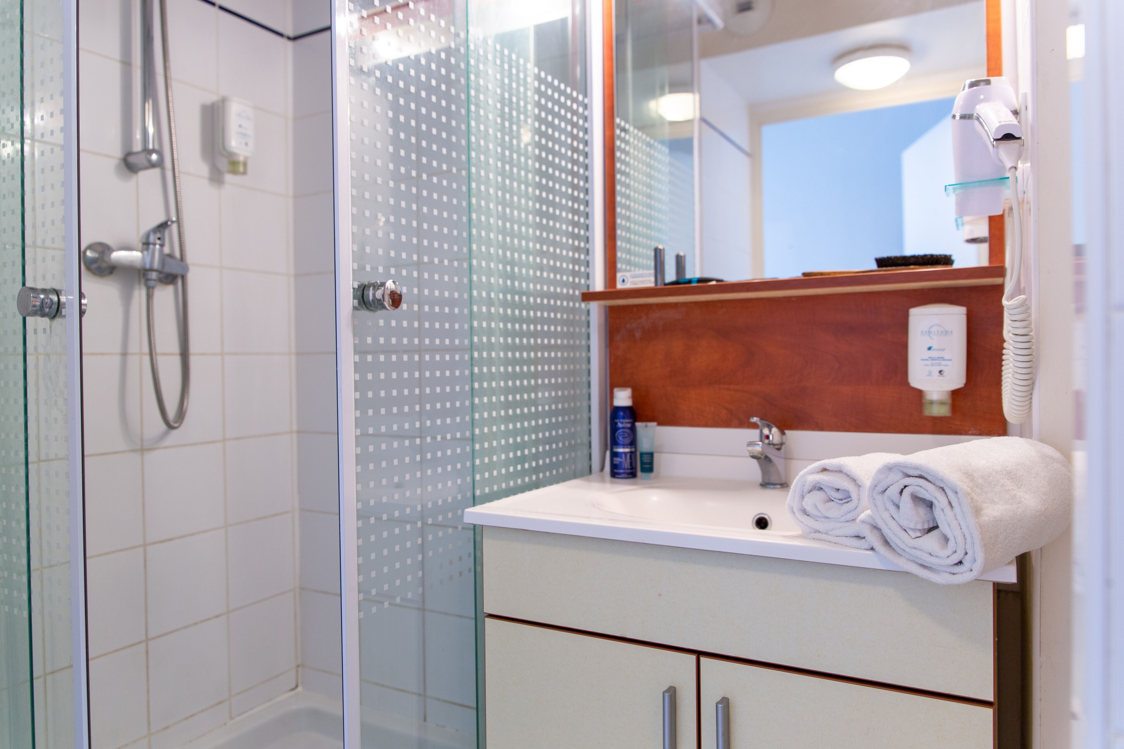 Een badkamer met een glazen douchecabine, een wit wastafelmeubel met een houten blad en een spiegel erboven.