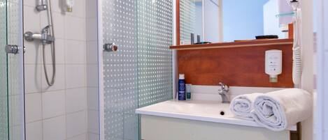 A bathroom with a glass shower enclosure, a white sink with a wooden countertop, and a mirror above the sink.