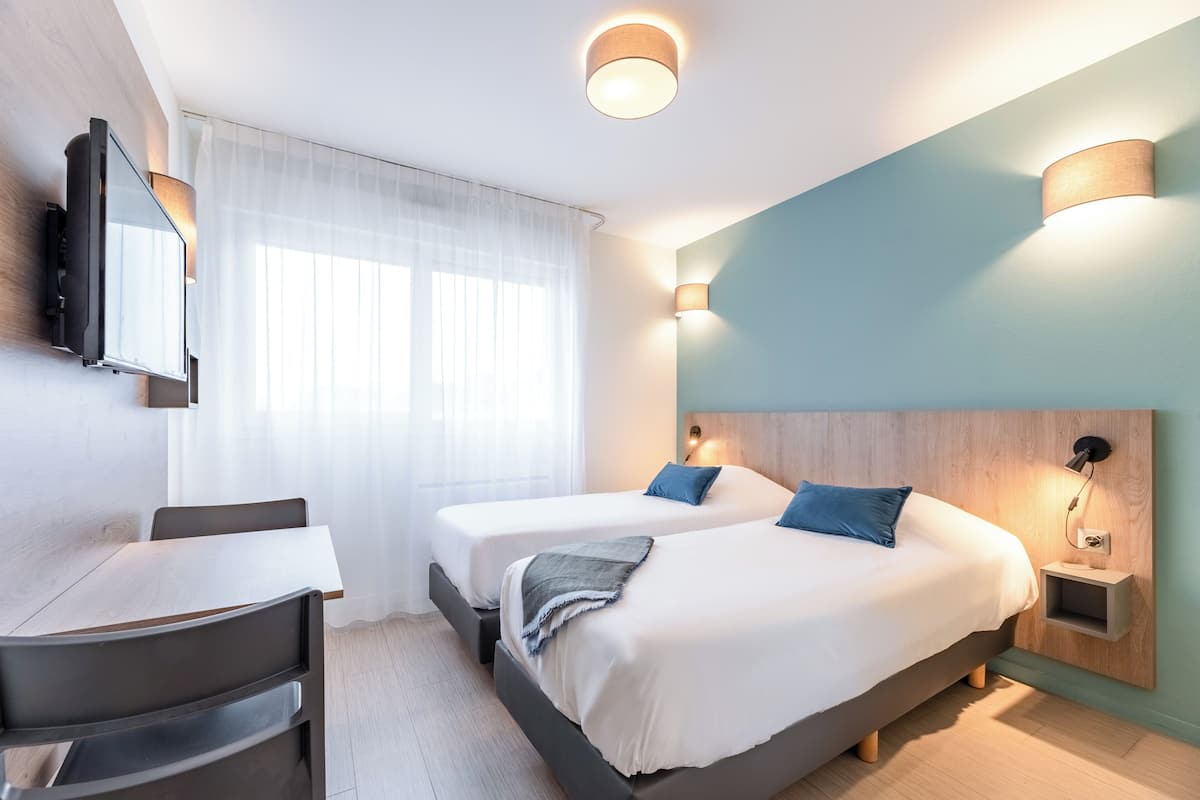 A modern hotel room with two beds, a desk, and a TV.