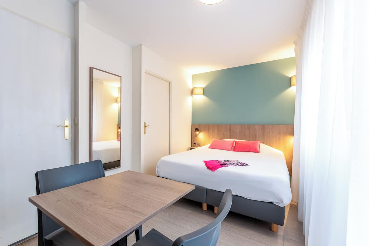 A hotel room with a bed, bedside table, and a mirror.