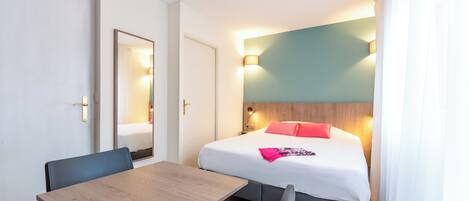A hotel room with a bed, bedside table, and a mirror.