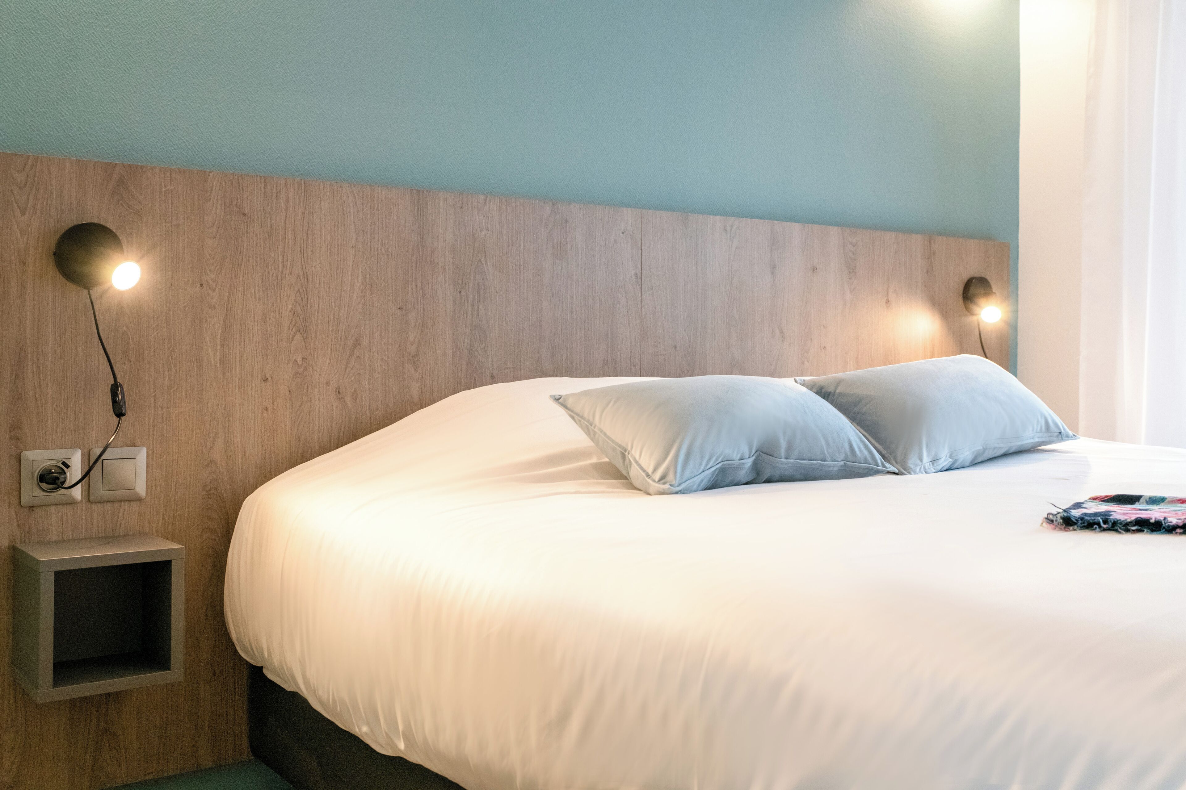 Un letto rifatto con due cuscini, una testiera in legno e lampade ai comodini.