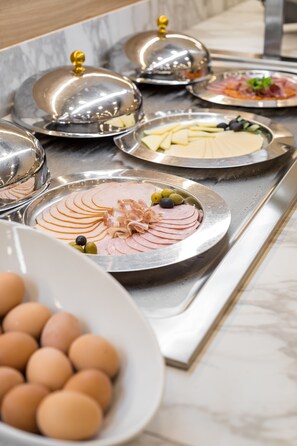 A buffet setup with various dishes, including sliced meats and cheeses, covered with silver domes.