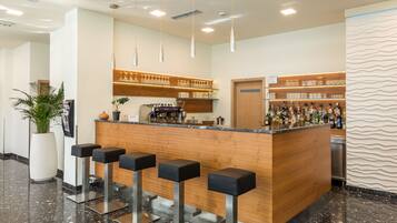 A bar area with a wooden counter, black bar stools, and shelves of bottles and glasses.