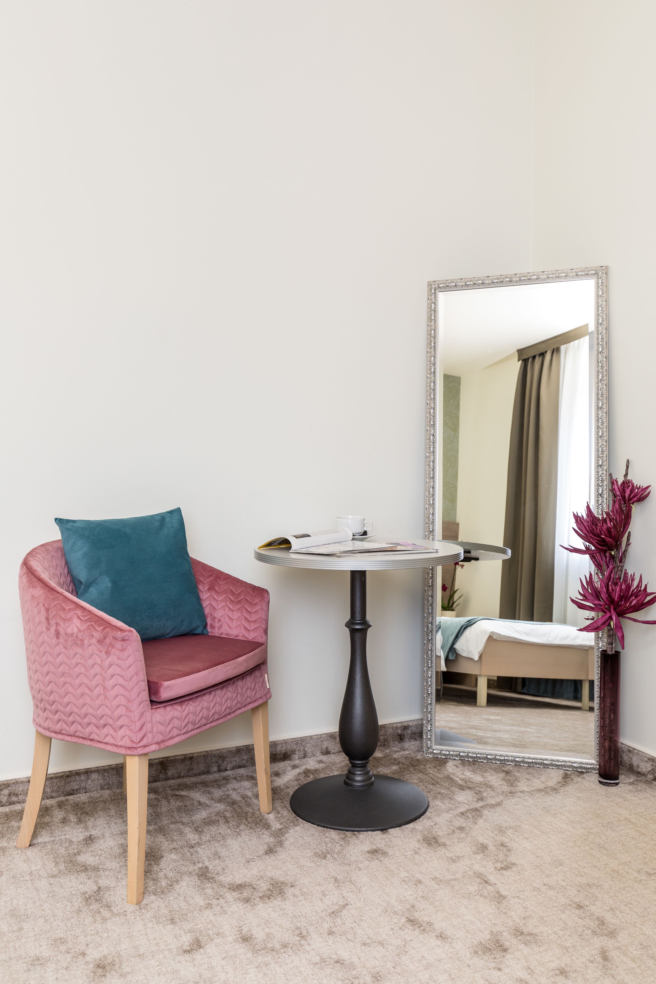 A room with a pink chair, a round table, a mirror, and a potted plant.