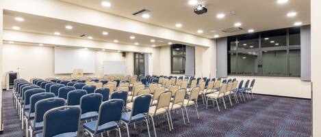 A conference room with rows of chairs, a whiteboard, and a projector screen.
