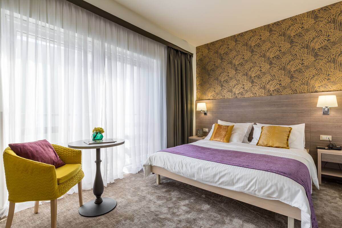 A hotel room with a bed, a chair, a small table, and a lamp.