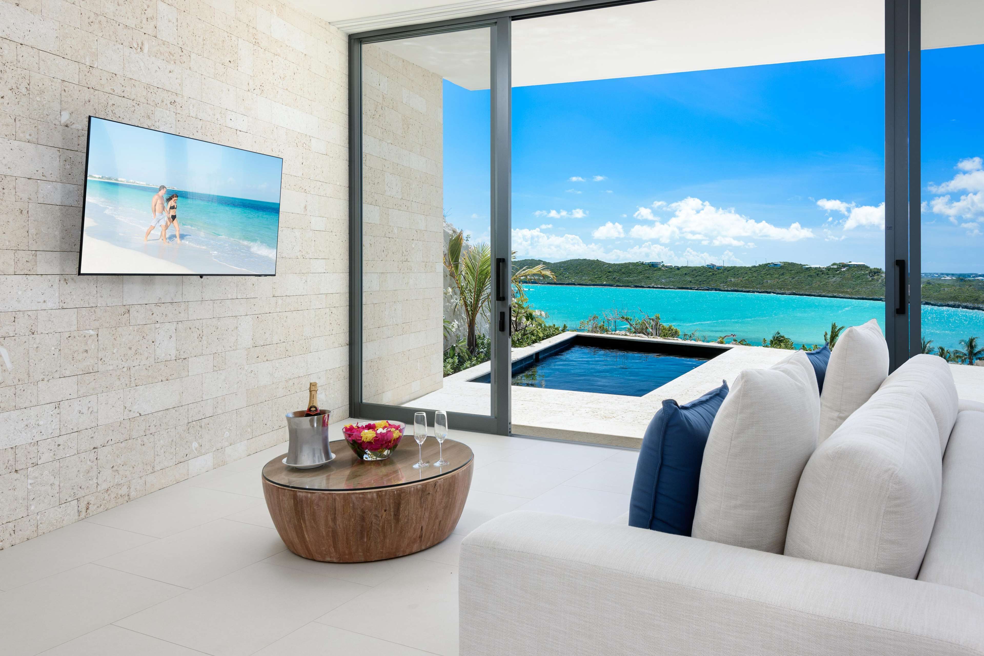 Un salon moderne doté d’une grande fenêtre donnant sur une piscine et une plage.