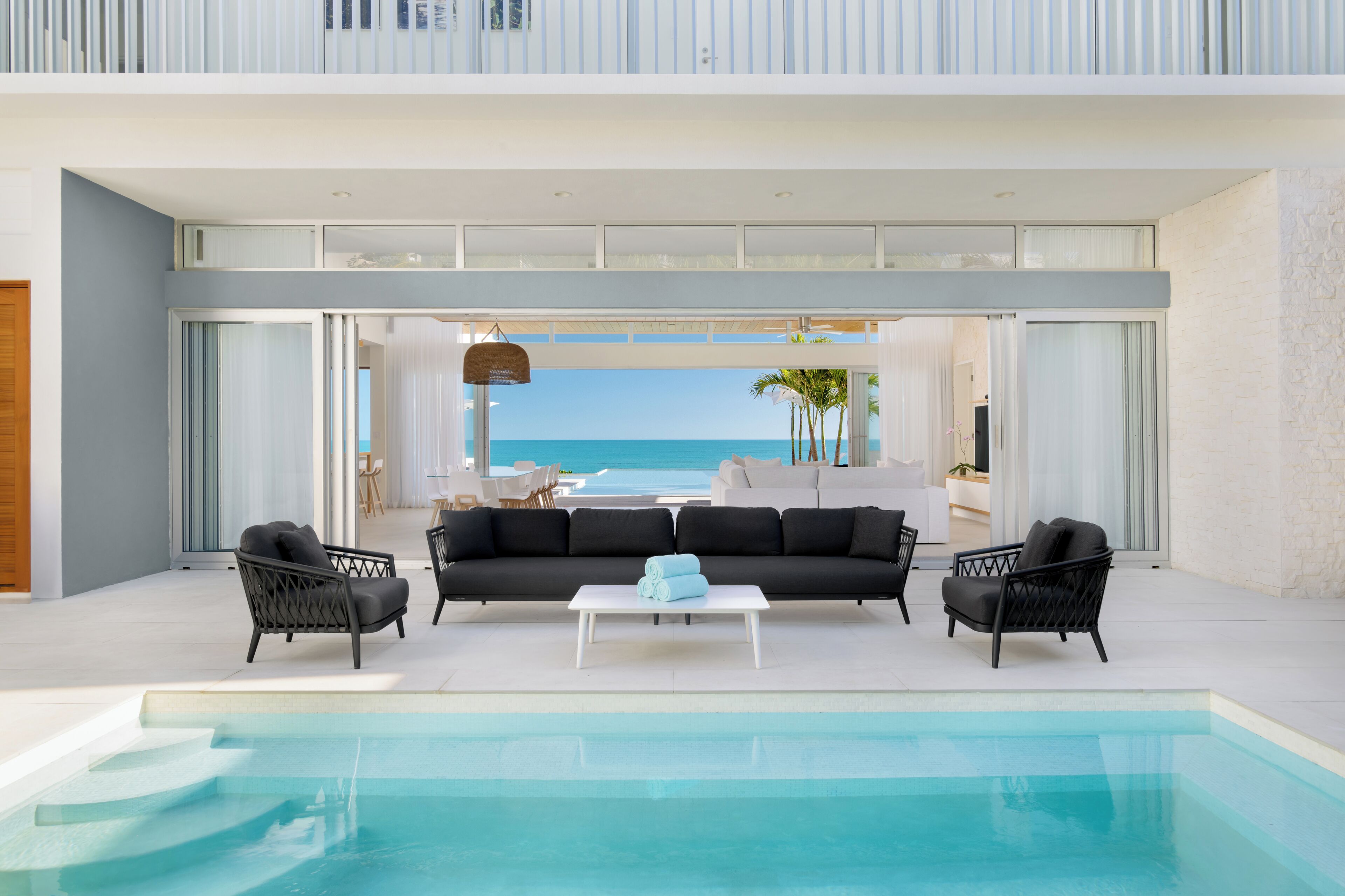 A modern outdoor living area with a pool, black sofas, and wicker chairs.