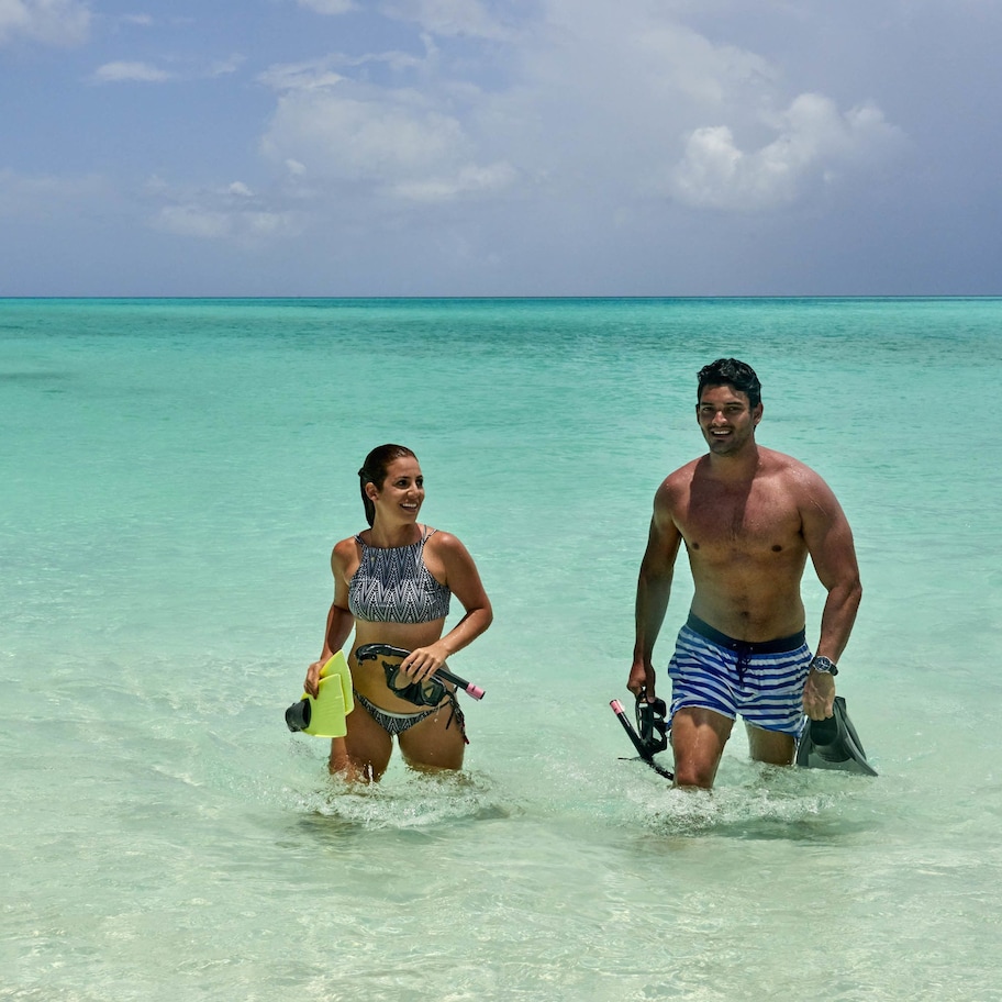 Two people in shallow water, one holding a snorkel and fins, and the other holding a camera.