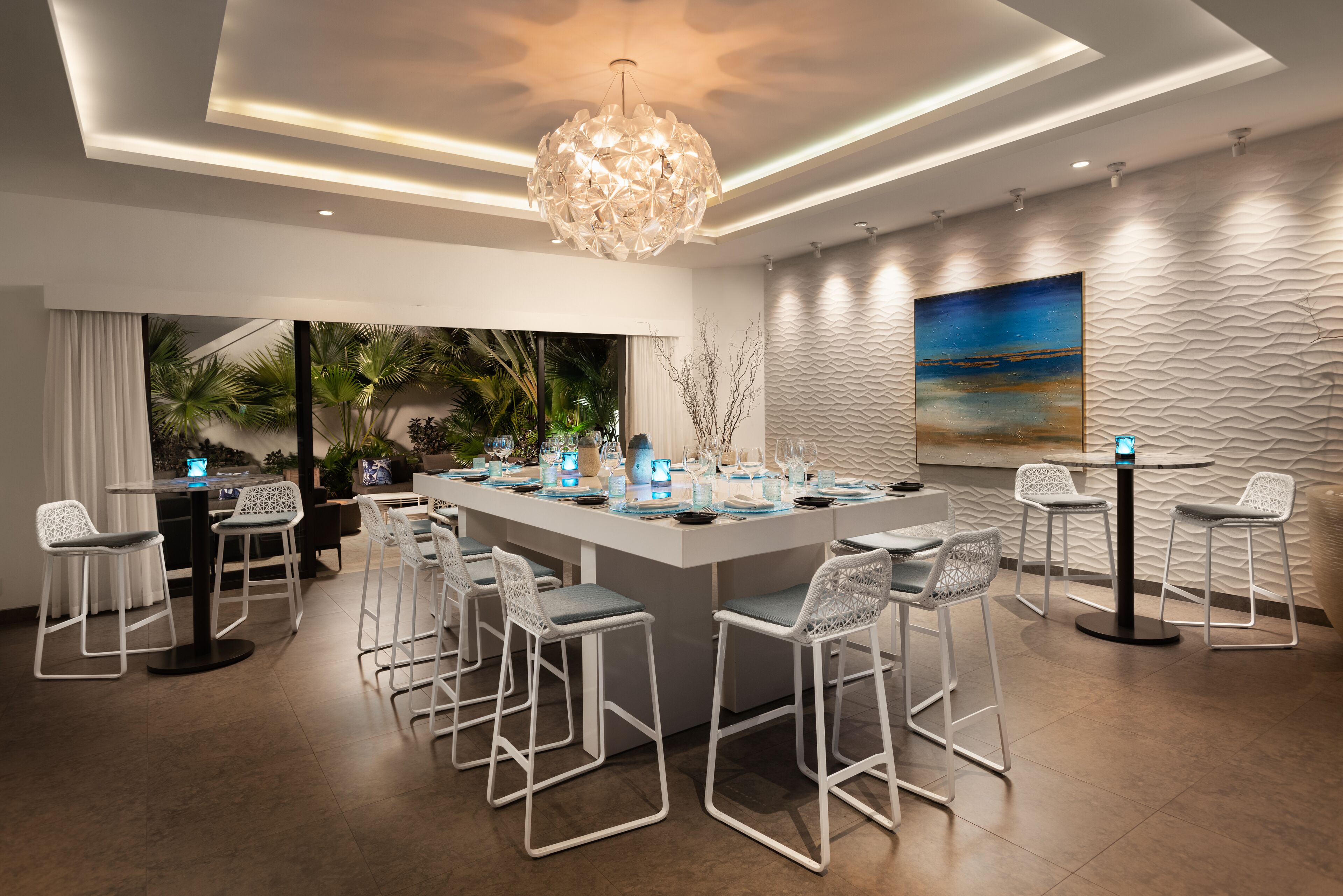 Zona de bar moderna con una isla central, taburetes blancos y una lámpara decorativa.