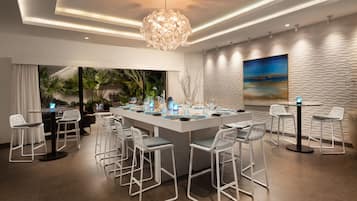 Zona de bar moderna con una isla central, taburetes blancos y una lámpara decorativa.
