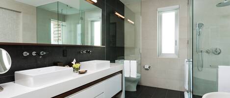 A modern bathroom with a large mirror, two sinks, a glass shower enclosure, and a toilet.