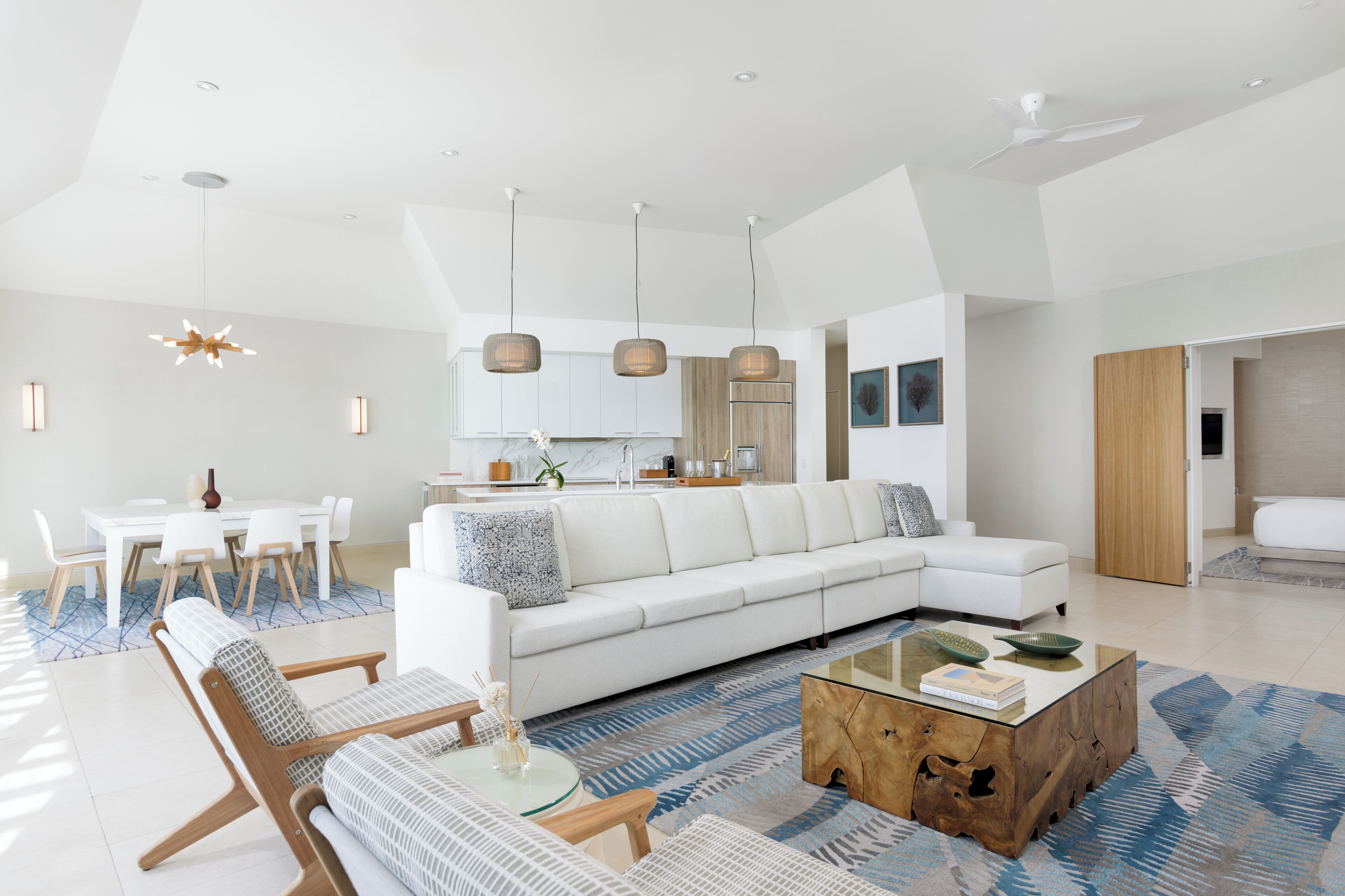 Una sala de estar moderna con un sofá seccional blanco, una mesa de centro de vidrio y un comedor con mesa y sillas blancas.