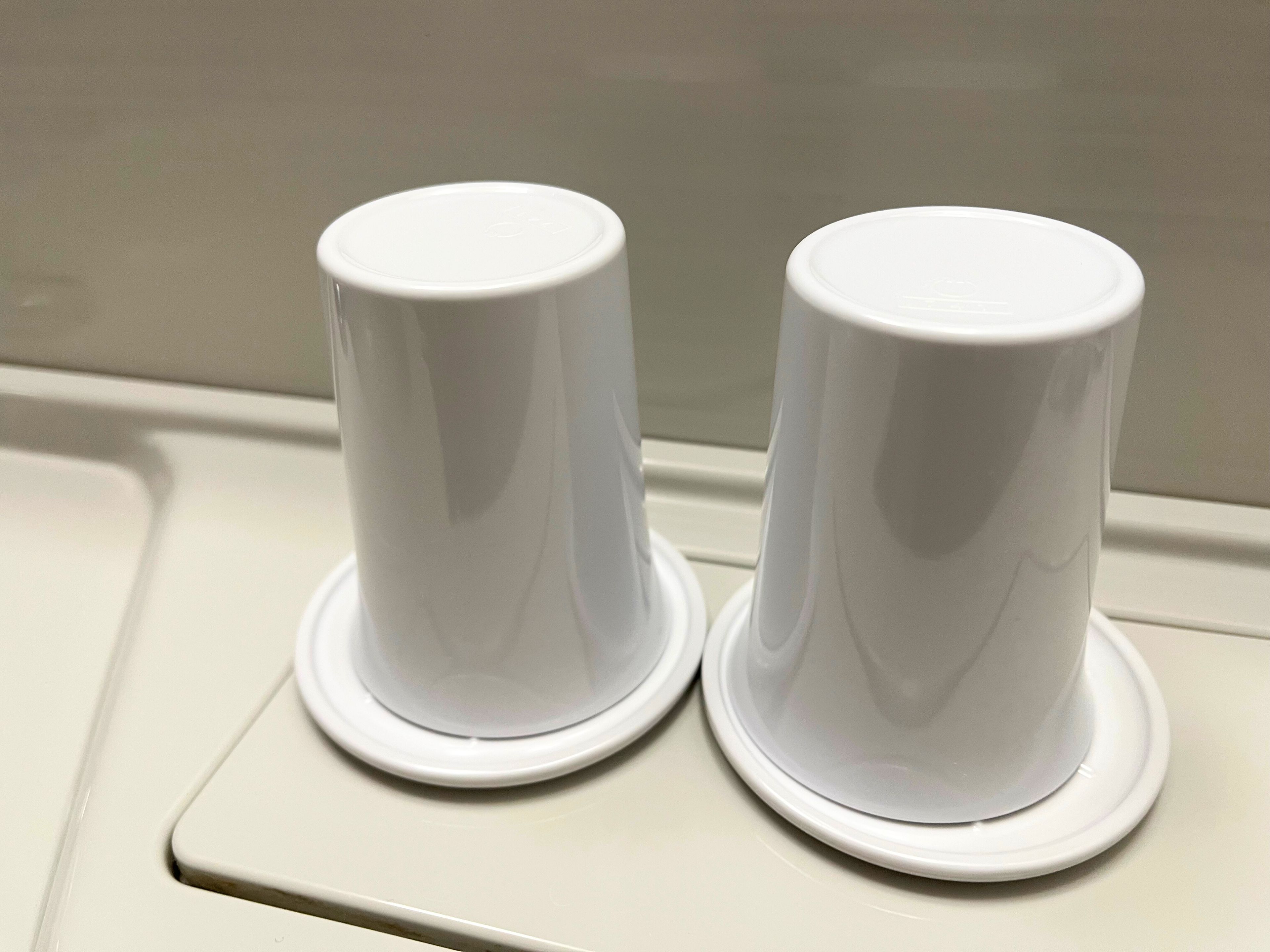 Two white cylindrical objects with bases, likely soap dispensers, on a white surface.
