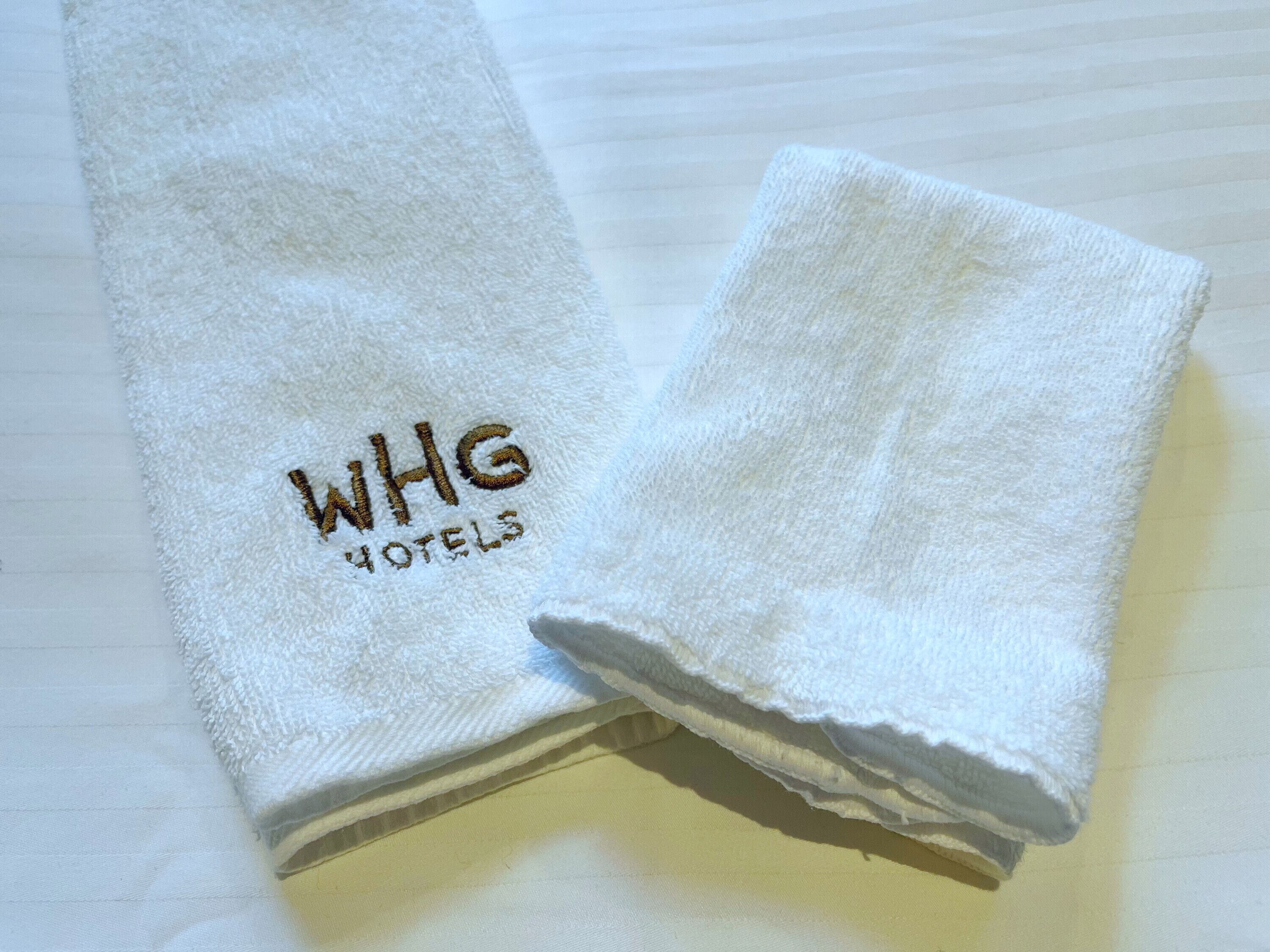 Zwei weiße Handtücher mit eingesticktem Text "WHG HOTELS".