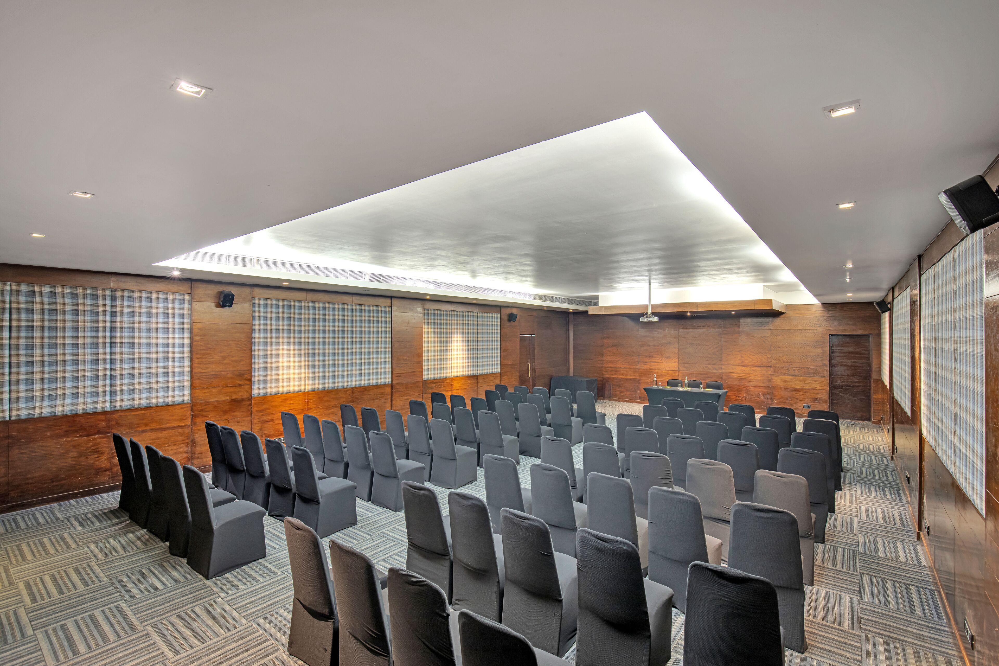 Un salón de conferencias con filas de sillas, una mesa grande y un techo alto con tragaluces.