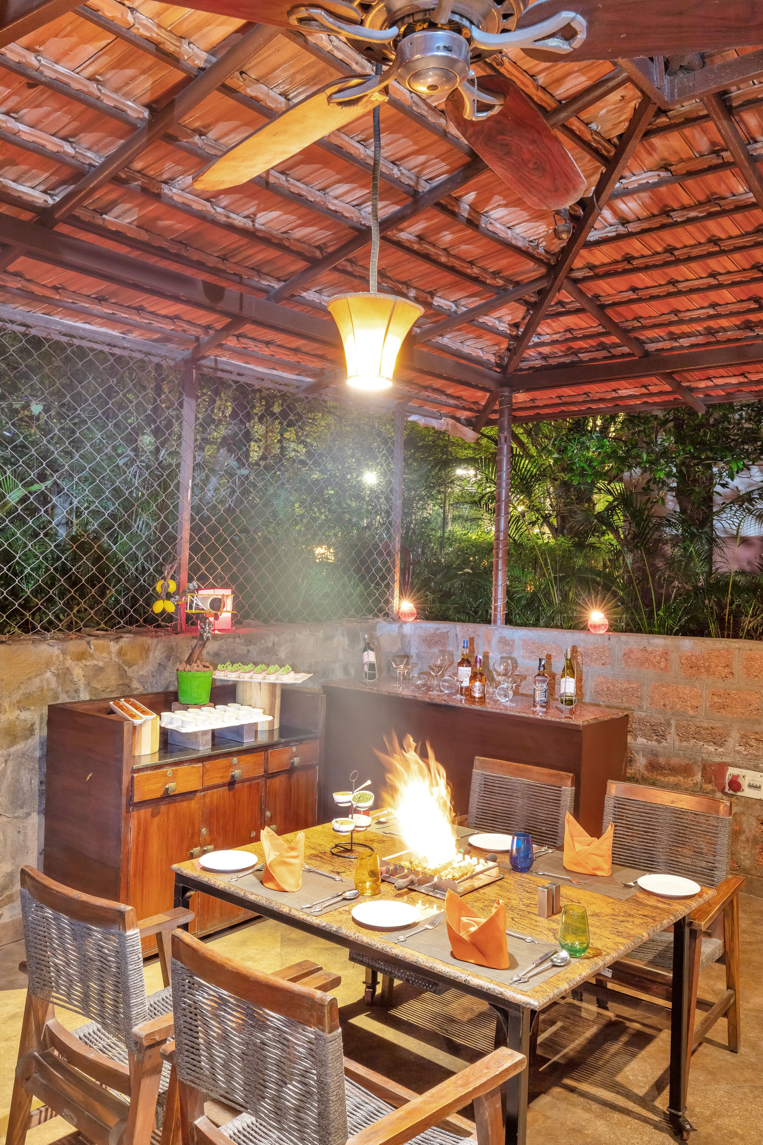 Un área de comedor al aire libre con una chimenea, muebles de madera y diferentes tipos de mesas dispuestas.