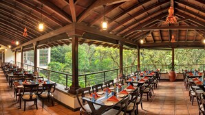 A covered outdoor dining area with wooden tables and chairs, large windows, and hanging light fixtures. - Club Mahindra Madikeri, Coorg (Madikeri)