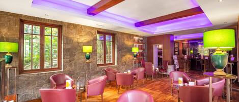A spacious lounge area with wooden flooring, stone walls, and multiple seating areas with purple chairs.