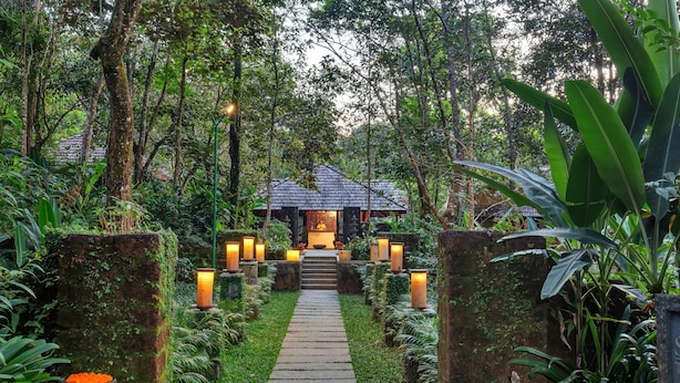 A pathway leading to a traditional-style building surrounded by lush greenery and stone walls. - Club Mahindra Madikeri, Coorg (Madikeri)