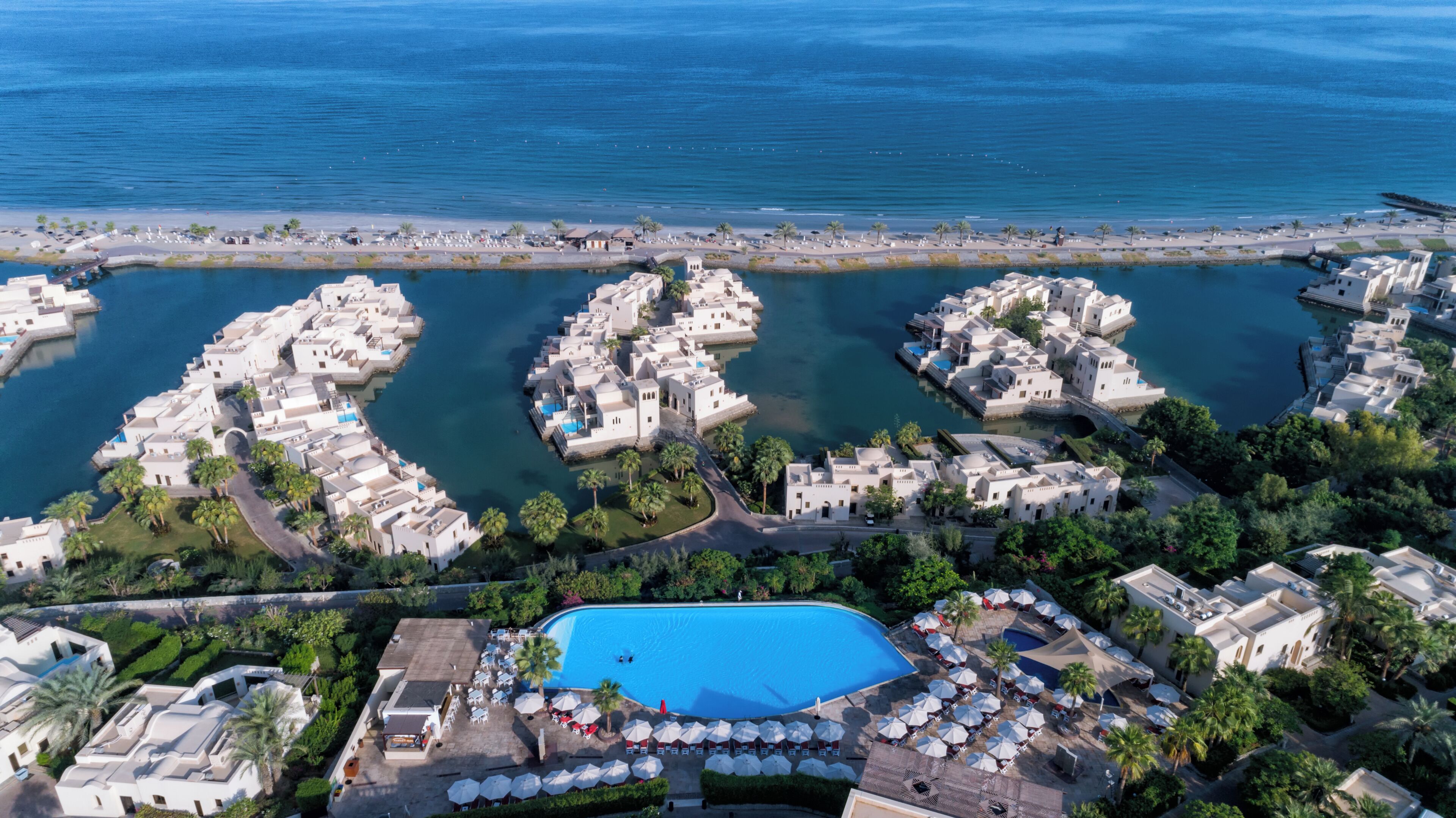 Vue aérienne d’une station balnéaire comprenant plusieurs villas, une piscine centrale et une plage.