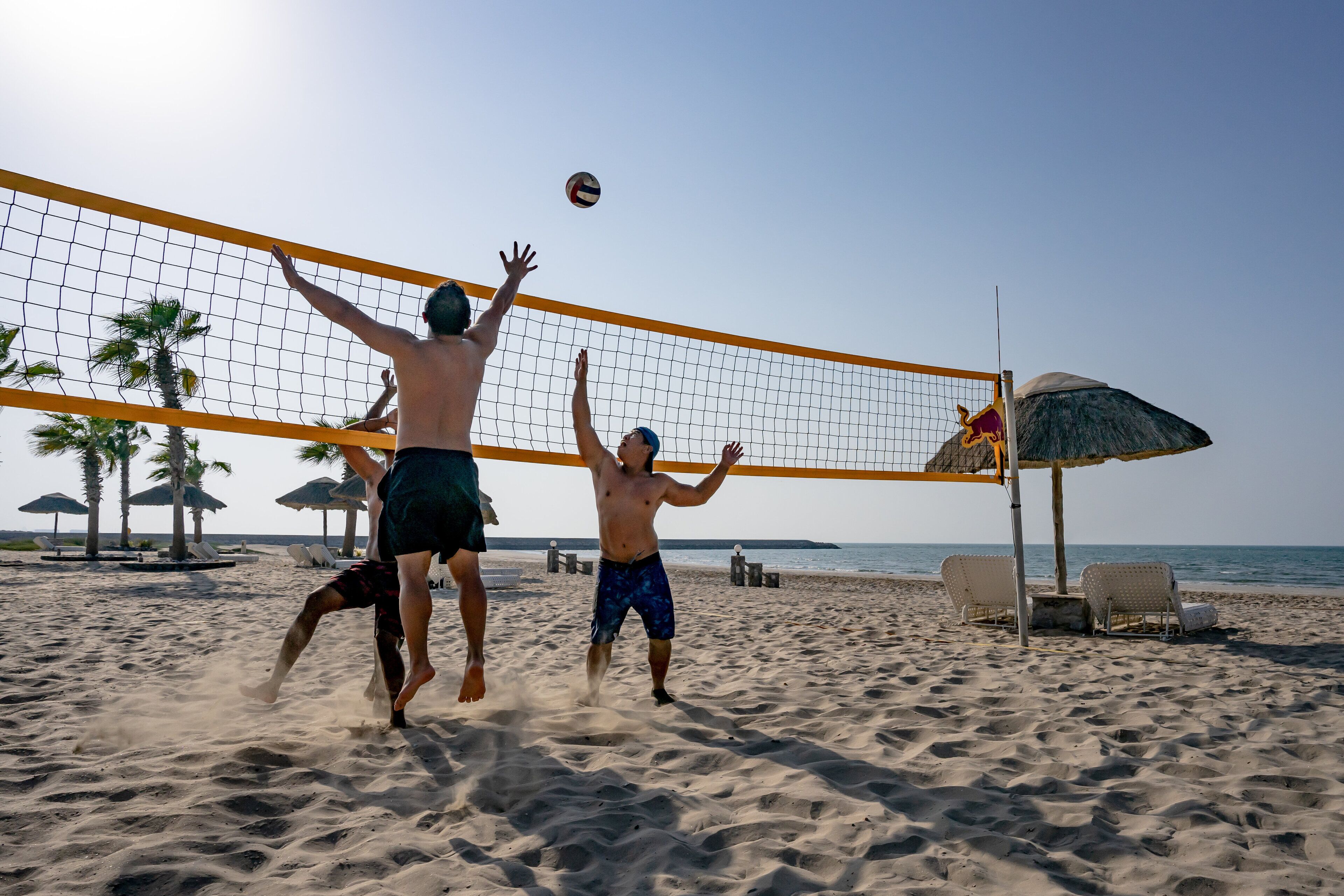 Een strandvolleybalwedstrijd met een net en palmbomen op de achtergrond.