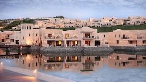 Un hotel costero con varias edificaciones, una piscina reflectante y vistas a una colina.