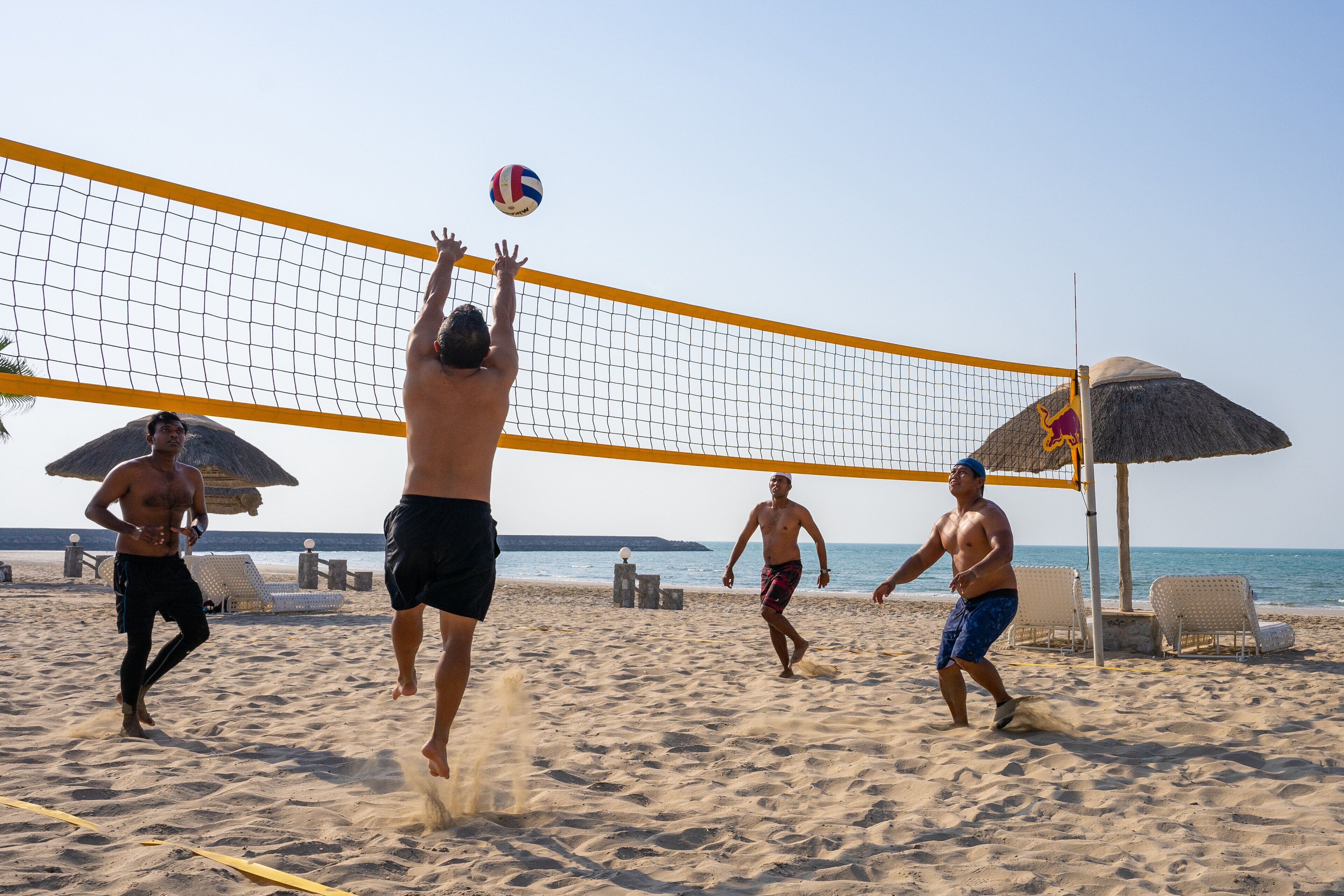 A beach volleyball game with players in shorts and a net in the middle.