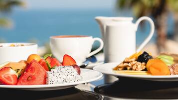 Une table avec des assiettes de fruits et une tasse de café, le tout sur un fond flou représentant une plage et des palmiers.