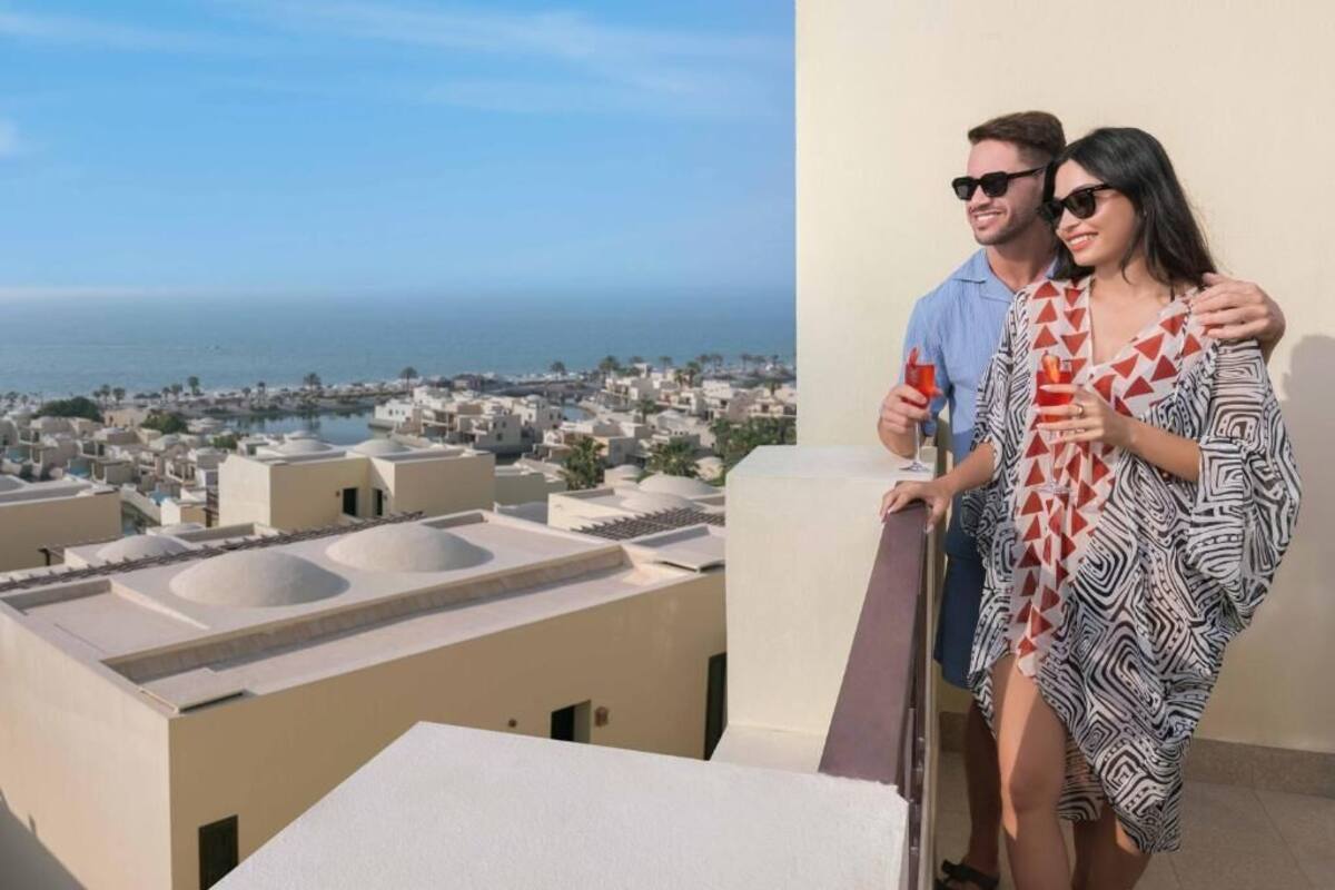 A couple on a balcony overlooking a coastal cityscape.