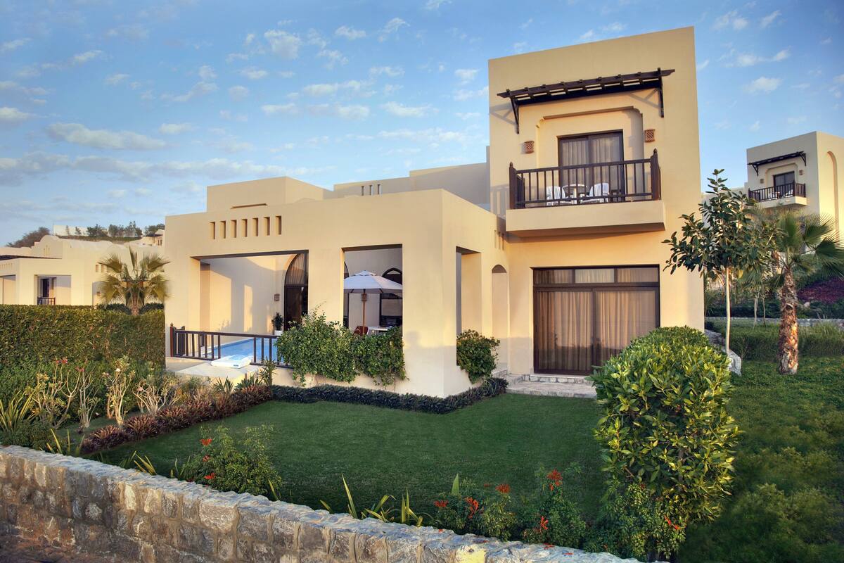 A modern two-story house with a balcony, a swimming pool, and well-maintained gardens.