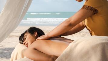 A person receiving a back massage on a beach with ocean in the background.