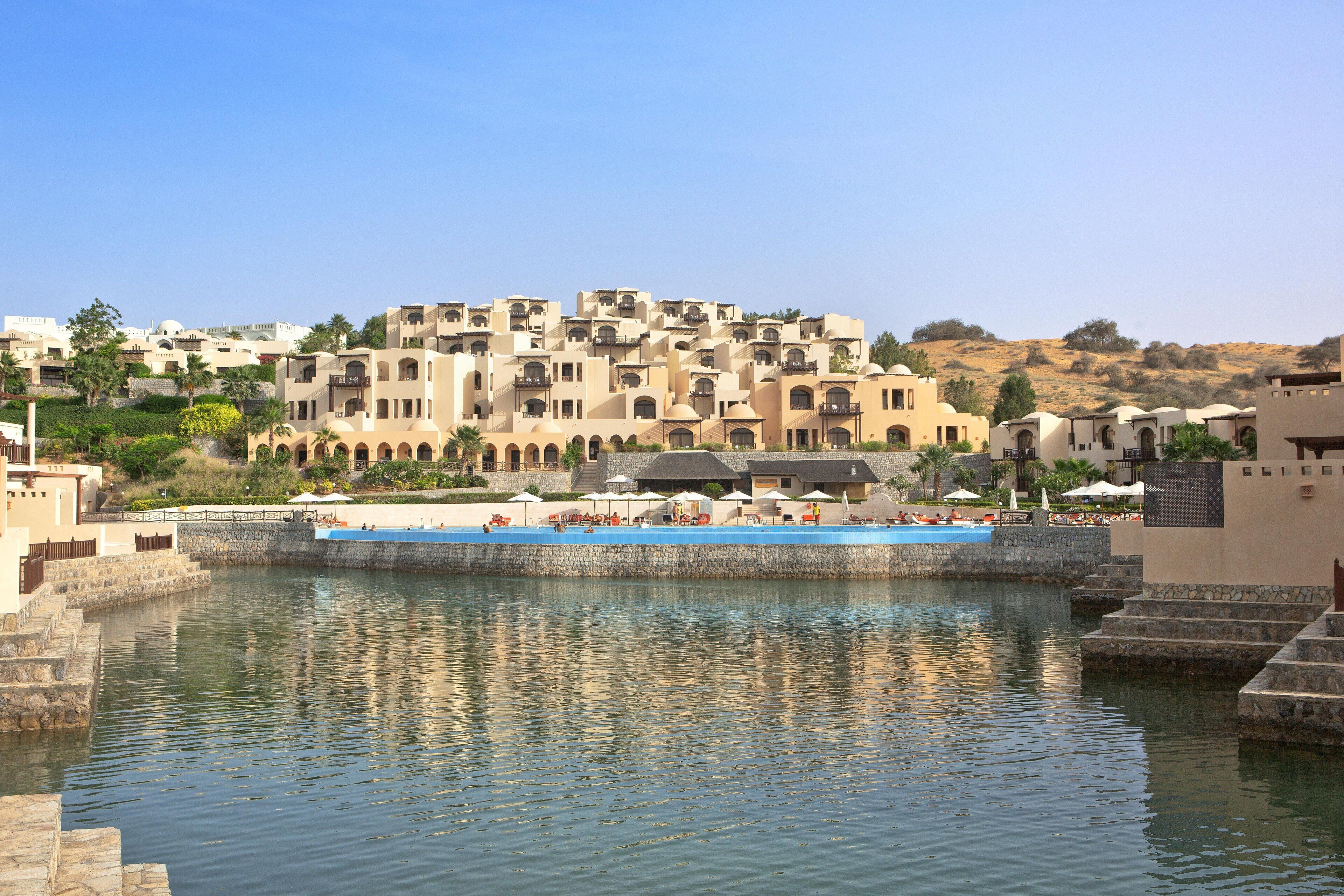 Un resort con zona de piscina, varias construcciones con balcones y un paisaje montañoso de fondo.