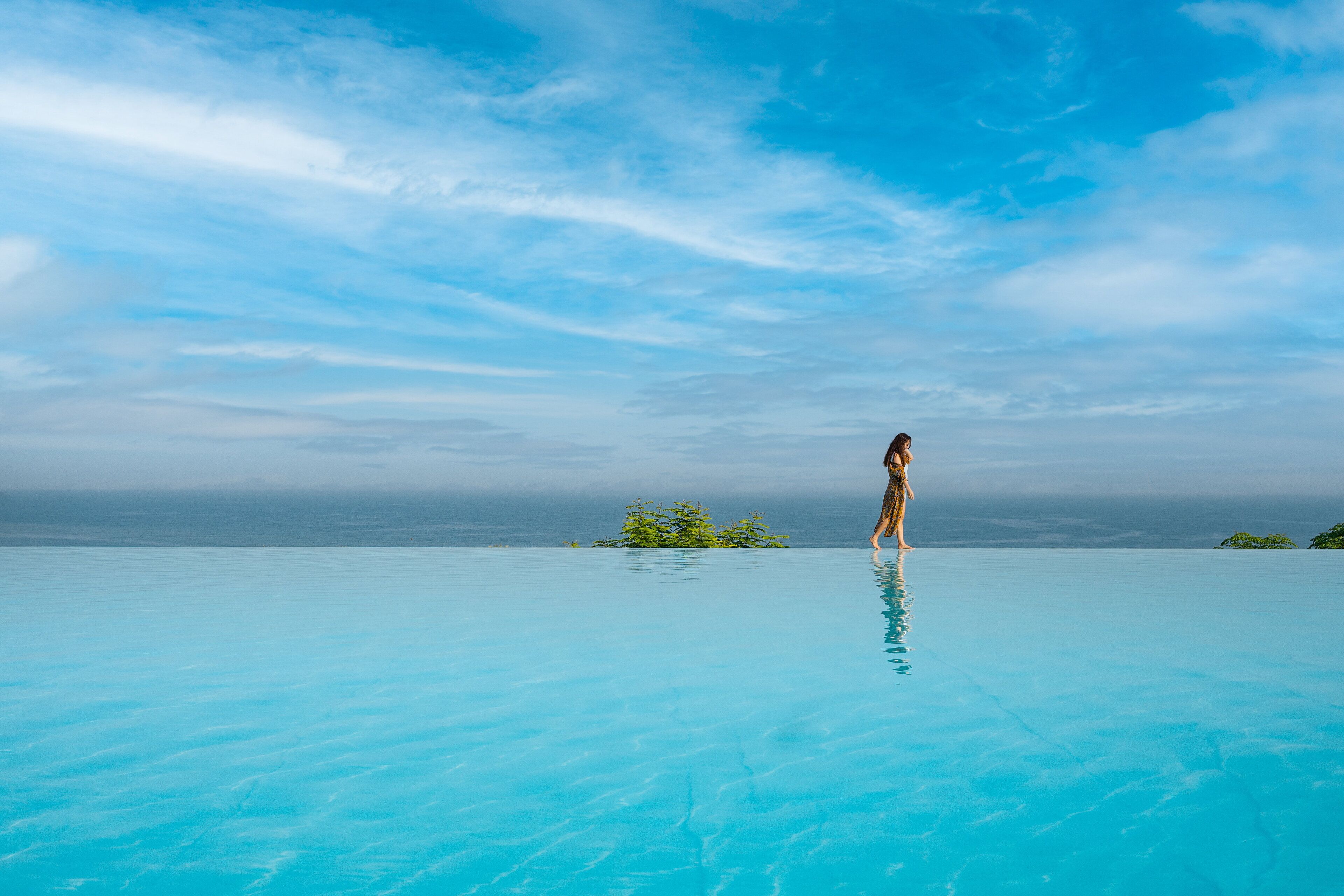 A person standing on a clear blue infinity pool with a view of the ocean and sky.