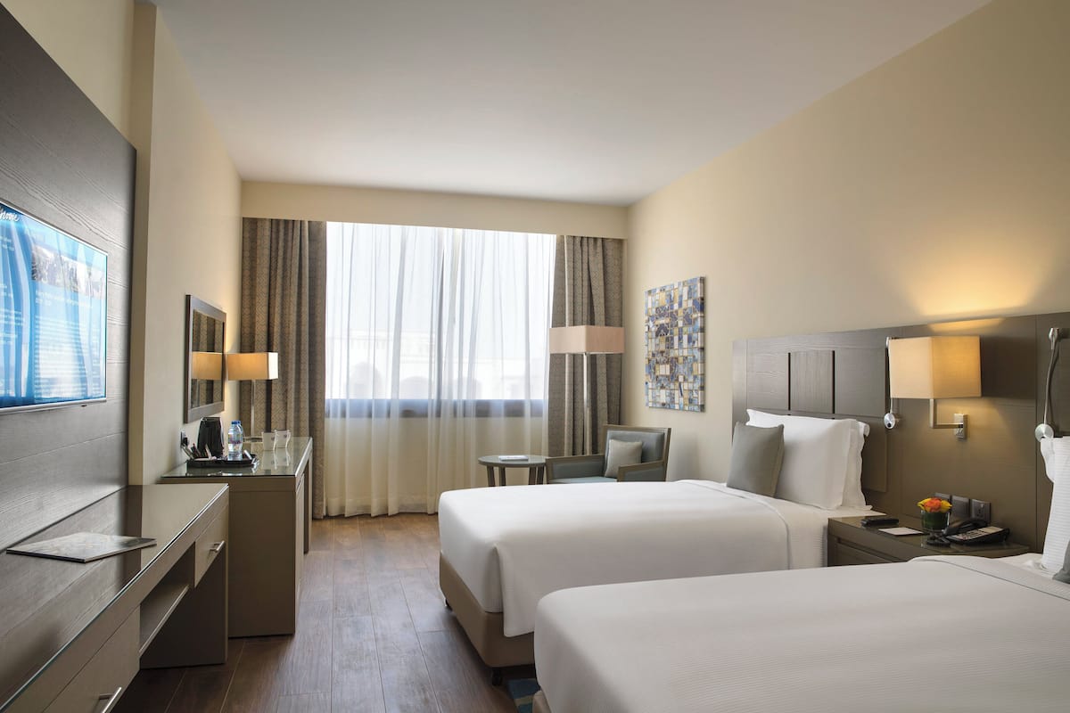 A hotel room with two beds, a desk, a chair, a small table, and a window with curtains.
