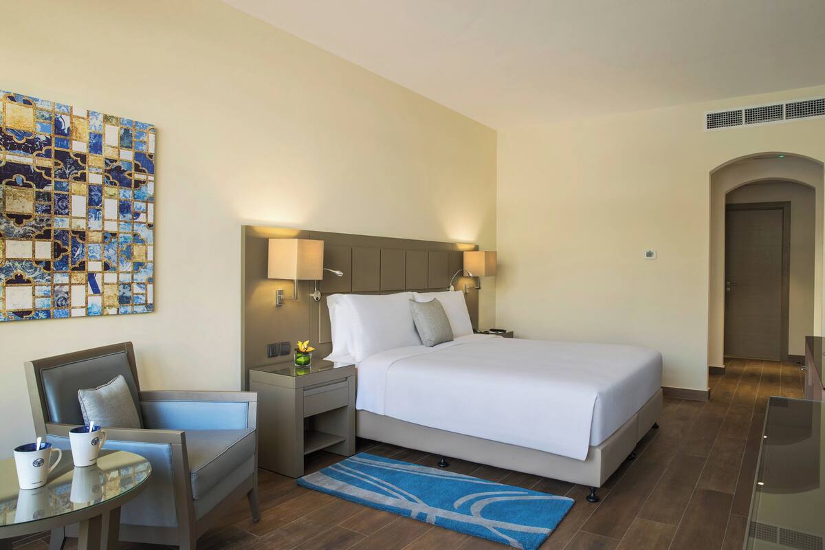 A hotel room with a bed, nightstands, a seating area, and a wall art piece.