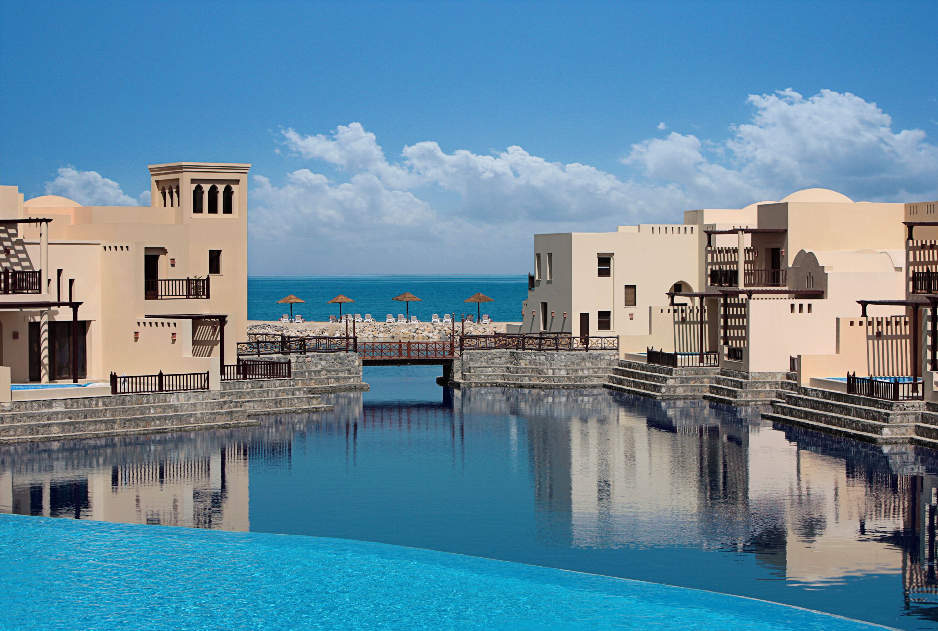 A pool area with a bridge, clear blue water, and a view of the sea.