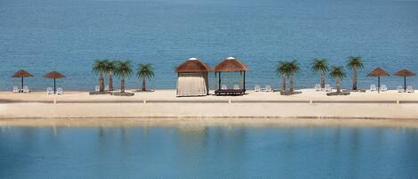 A beachside resort with a pool, palm trees, and beach chairs.