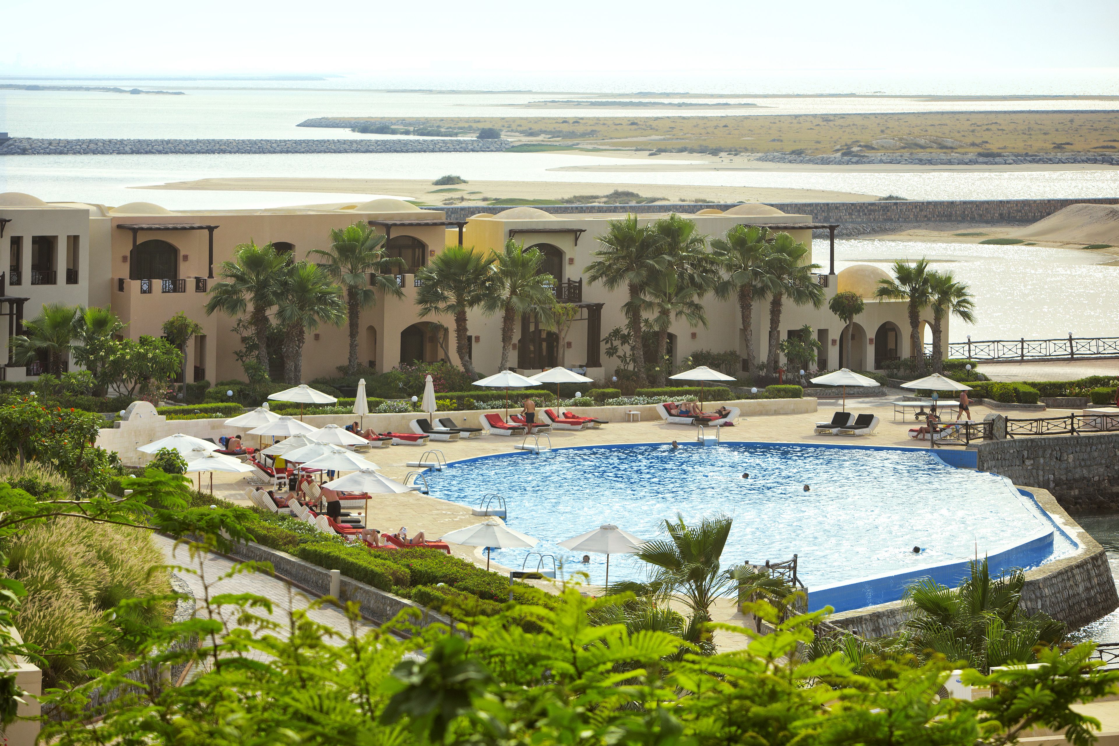 Ein Resort mit großem Pool, Palmen und Blick auf den Strand.