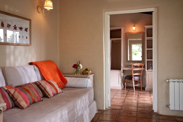 A cozy living room with a sofa, a small table with a vase of flowers, and a chair. There is a doorway leading to a kitchen area with a chair and a table. - House of Jasmines - Relais & Châteaux (Salta)