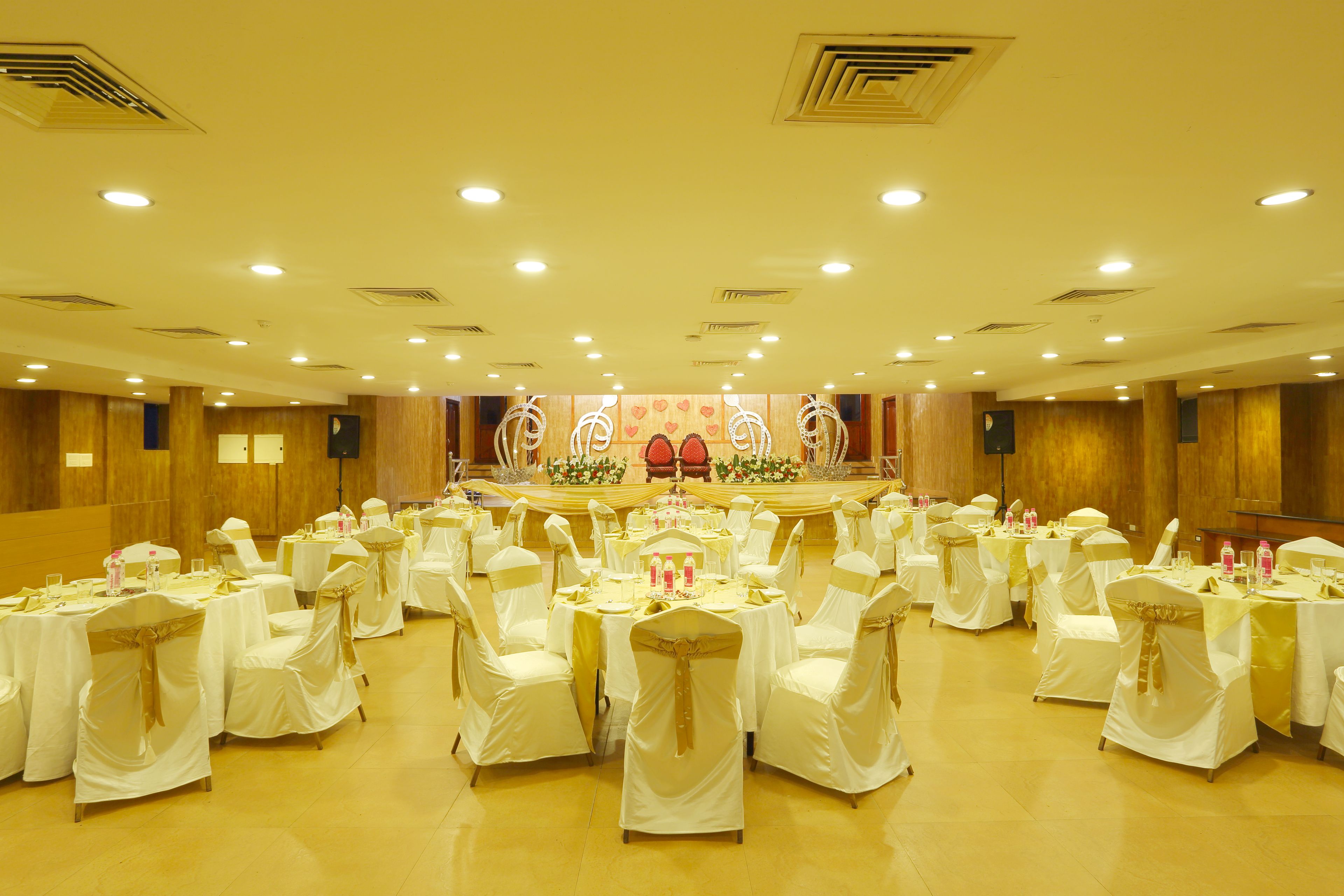 A banquet hall with round tables and chairs, a stage with a podium, and a large audience seating area.