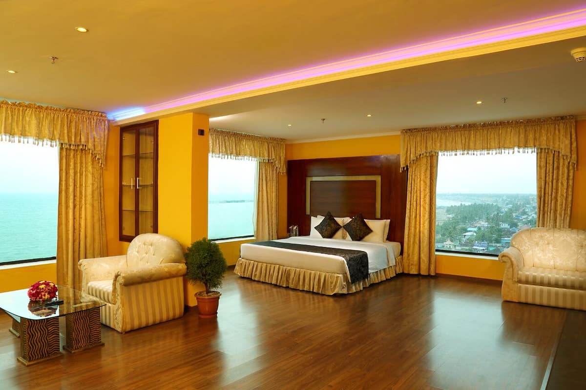 Amplia habitación de hotel con una cama grande, dos sillones, una mesita y vista al mar.