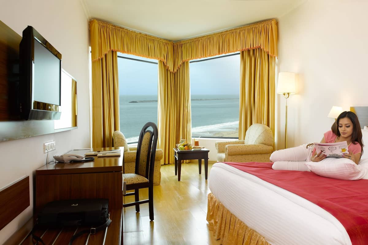 Habitación de hotel con cama, escritorio, silla, televisor y vista al océano.