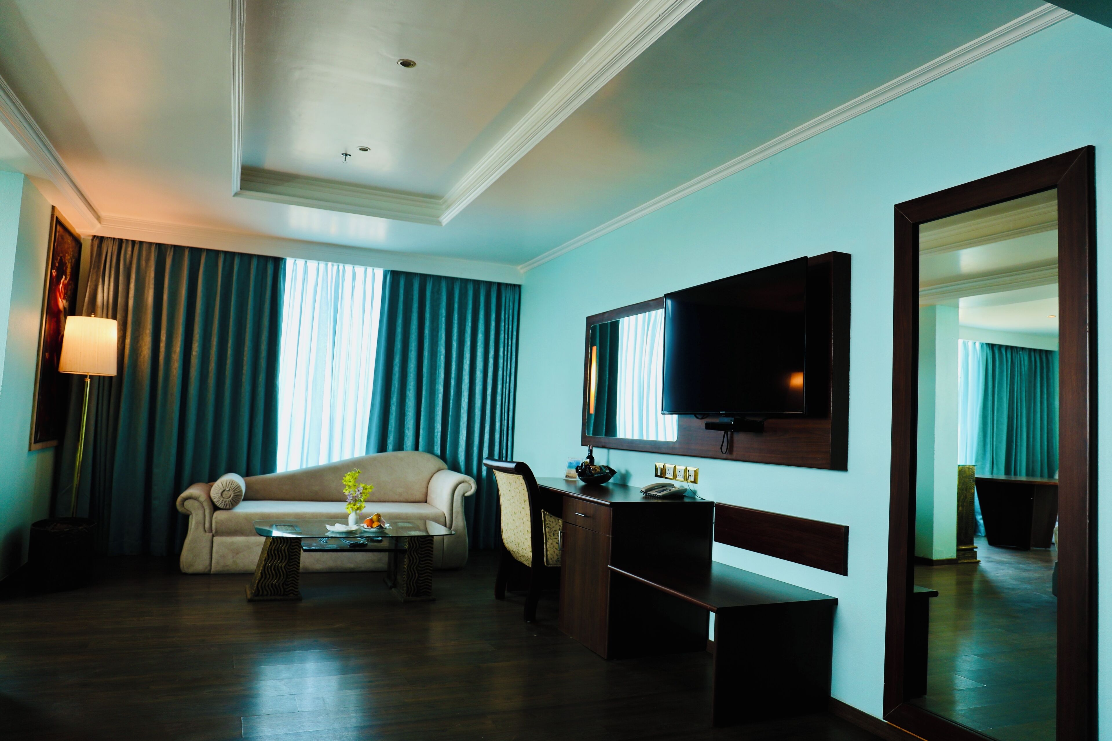 A hotel room with a sofa, a desk, a television, and a mirror.