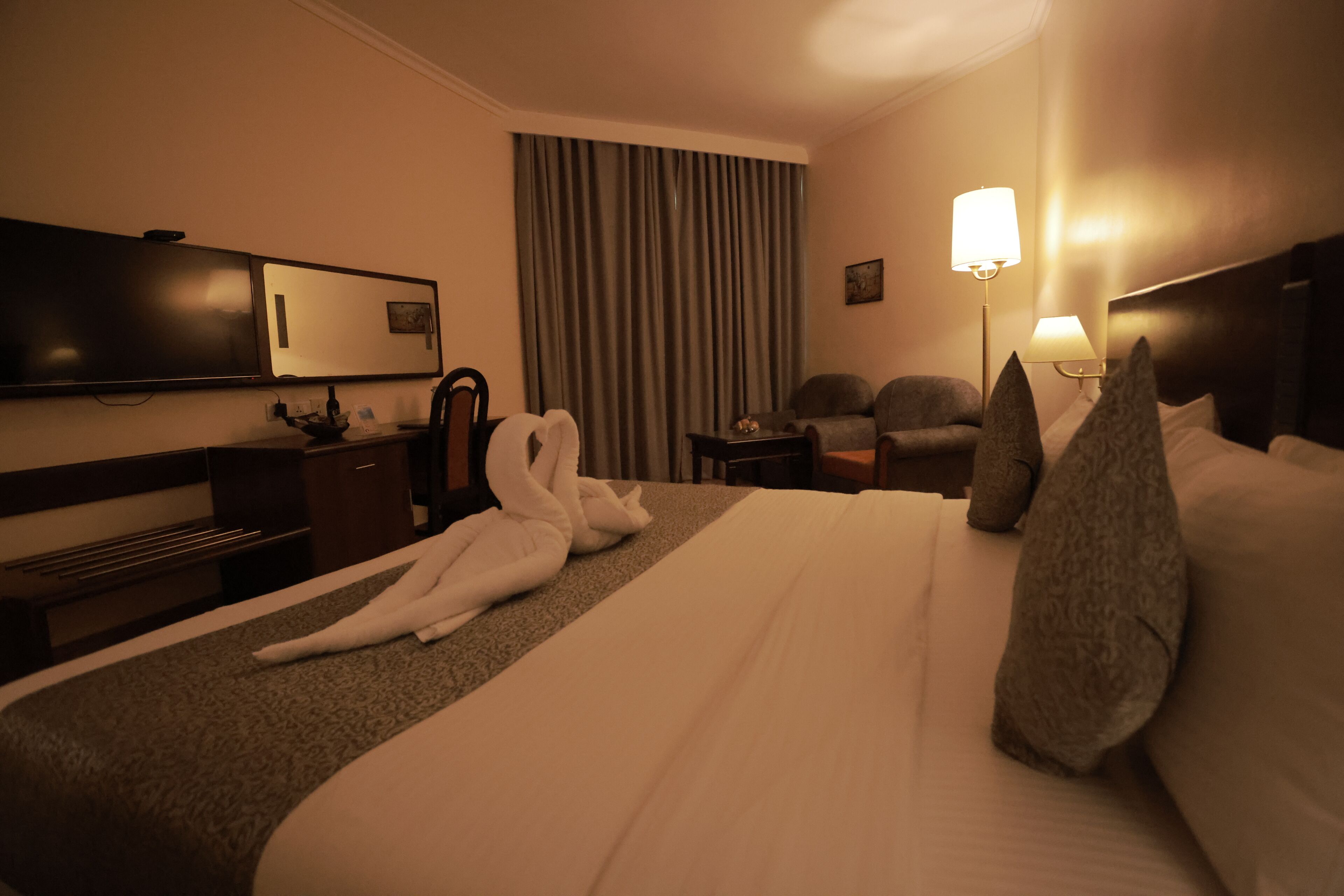 Una habitación de hotel con una cama grande, un escritorio, una silla, un televisor y una lámpara.