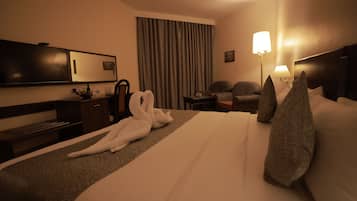 Een hotelkamer met een groot bed, een bureau, een stoel, een televisie en een lamp.